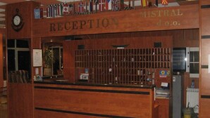 A reception desk with a wooden finish, a clock, and flags above it. - Aurora Hotel (Podgora)