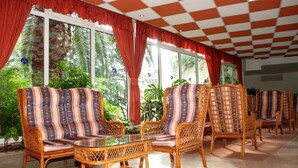 A room with wicker furniture, large windows, and a checkered ceiling. - Aurora Hotel (Podgora)