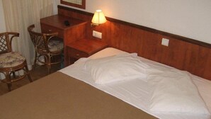 A hotel room with a bed, a desk, a chair, and a nightstand with a lamp. - Aurora Hotel (Podgora)