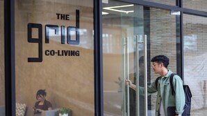 Une porte en verre sur laquelle on peut lire « The Grid Co-Living » et qui reflète l’image d’une personne à l’intérieur.
