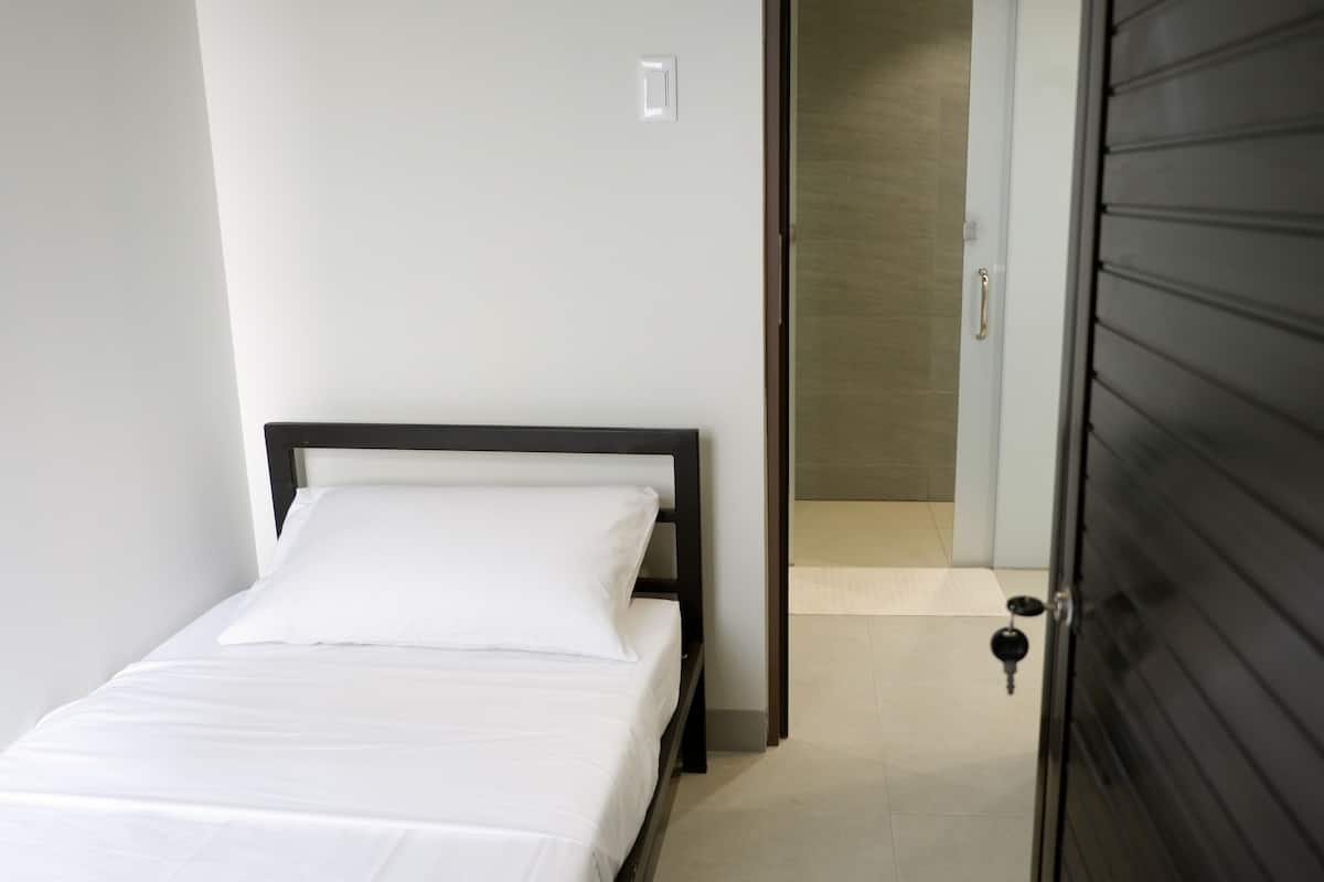 A small, neatly made bed in a room with a plain white wall and a closed door.