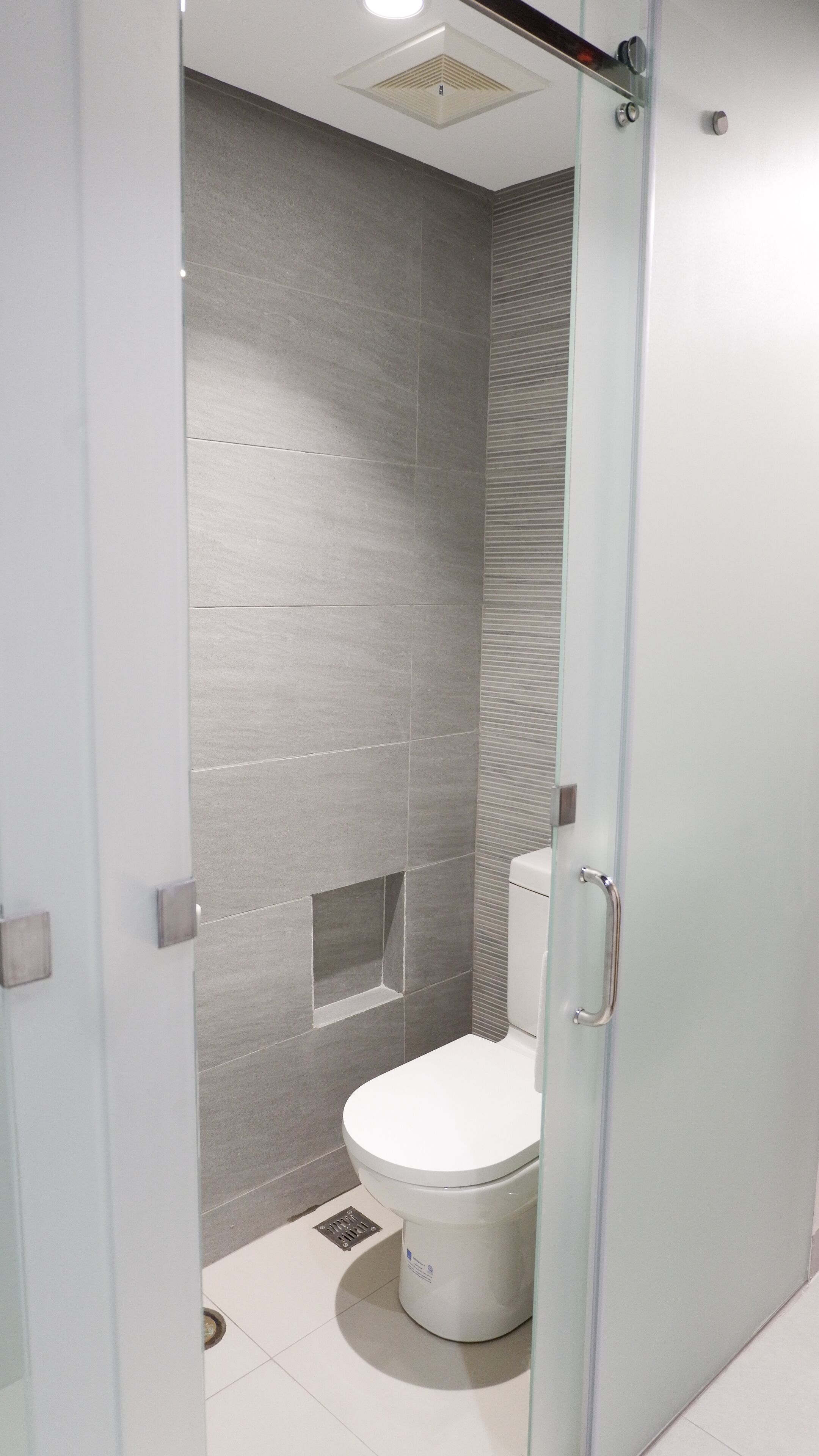 Ein modernes Badezimmer mit Glastrennwand, einer weißen Toilette und grauen Fliesen.