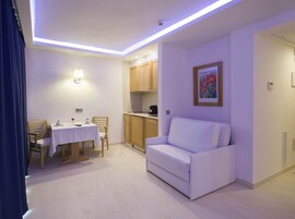 Una sala de estar moderna con un sofá blanco, una mesa de comedor con sillas y una zona de cocina.