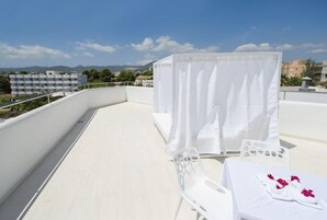 Una terraza en la azotea con una mesa blanca dispuesta para comer, una silla blanca y un dosel.