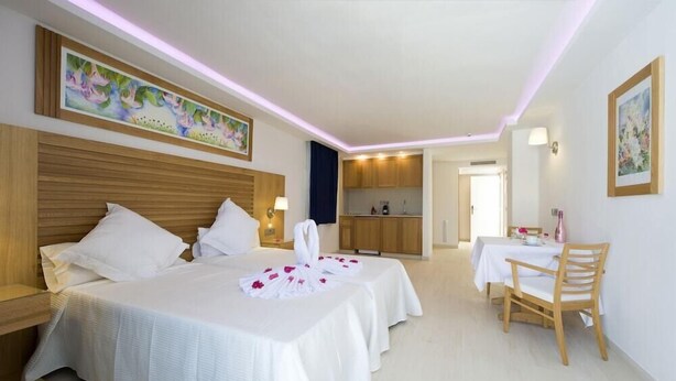 A hotel room with two beds, a small kitchenette, a dining table with a chair, and artwork on the walls. - My Way Luxury Ibiza (Sant Josep de sa Talaia)