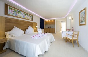 Habitación de hotel con dos camas, una kitchenette pequeña, una mesa de comedor con una silla y obras de arte en las paredes.