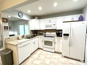 Una cocina moderna con armarios blancos, microondas integrado, estufa y refrigerador.