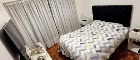 Ein Schlafzimmer mit einem Bett, einem Fernseher, einem Nachttisch und einer Klimaanlage.