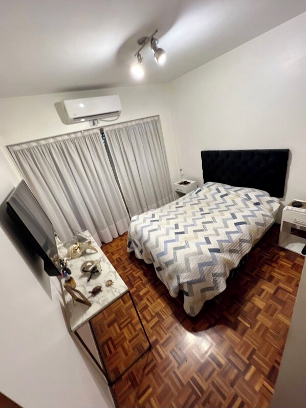 Une chambre à coucher comprenant un lit, un téléviseur, une table de chevet et un appareil de climatisation.