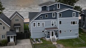 A two-story house with a front porch and a garage, located near a body of water with a sunset in the background.