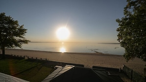 A beach view with a clear sky, a sun setting or rising over the water, and a fence in the foreground.