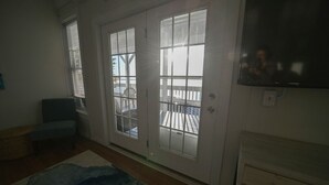 A room with a sliding glass door leading to a balcony, a television mounted on the wall, and a bench.