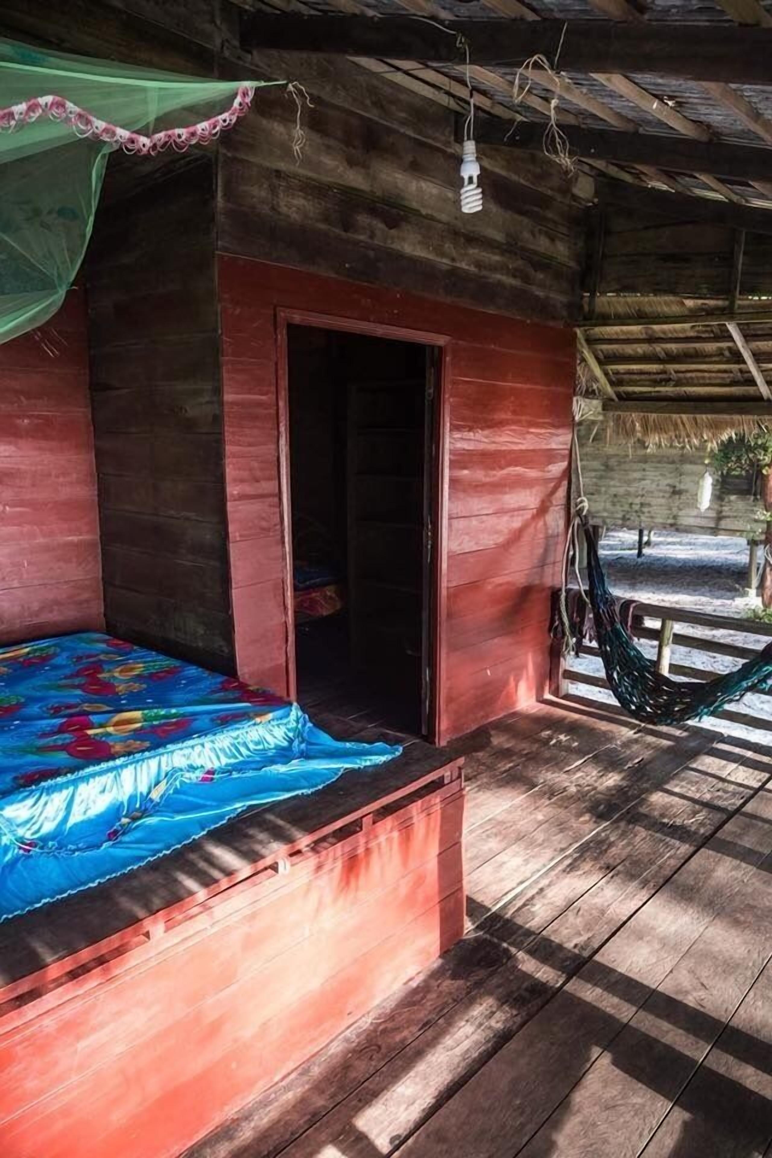 Una cabaña de madera con una cama, una hamaca y techo de paja.