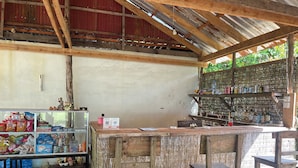 A rustic bar area with wooden furniture and shelves stocked with beverages. - Naks Shack (Prey Nob)
