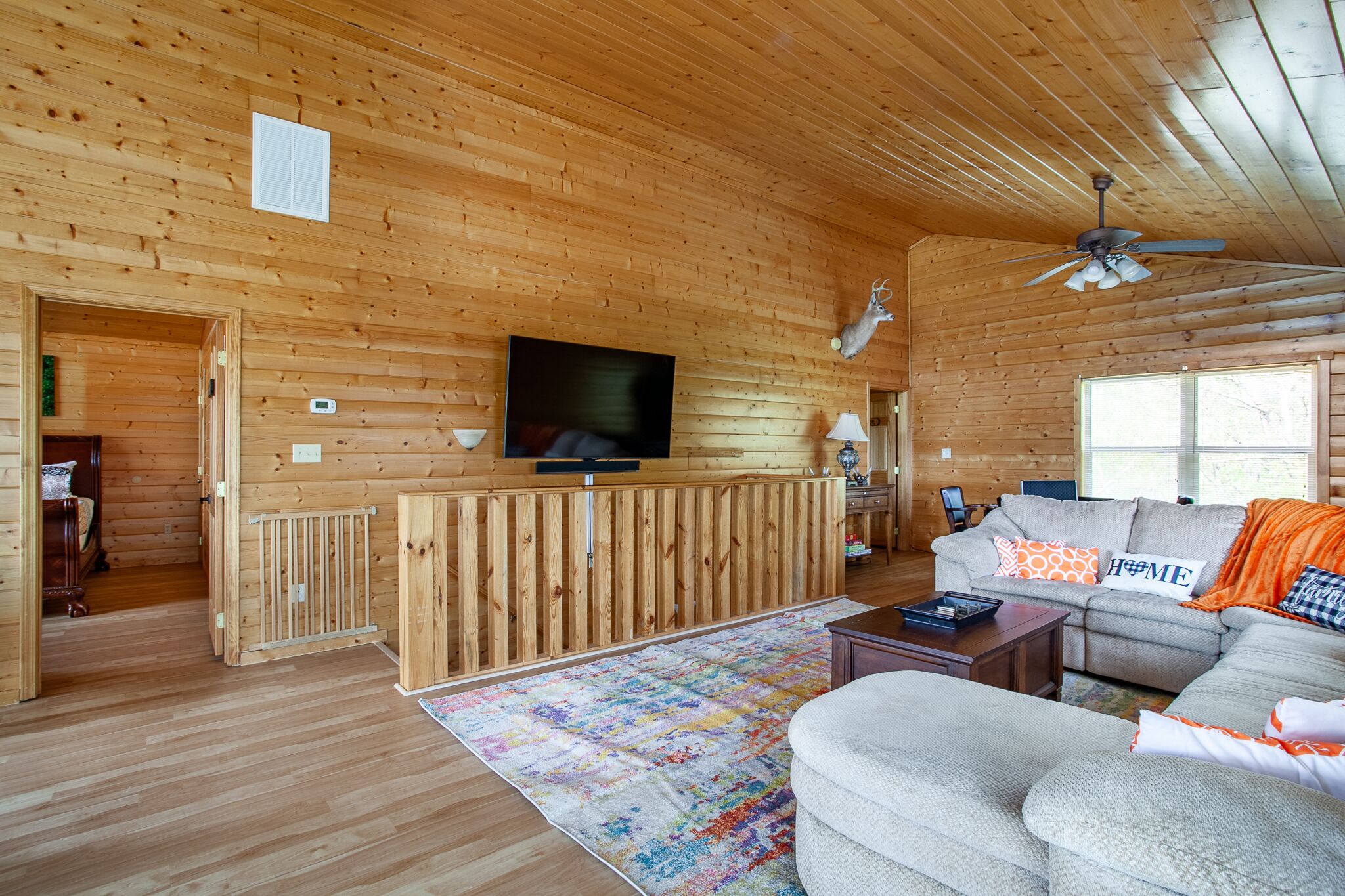 Een gezellig interieur van een chalet met een televisie, een open haard, een bank en een plafondventilator.