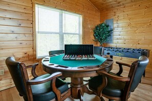 A wooden interior with a round table, four chairs, a foosball table, and a window with blinds. - Cozy Mountain Cabin I A++ Views & Amenities (Sevierville)