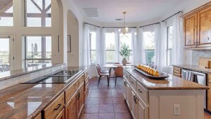 A modern kitchen with a central island, large windows, and a dining area. - Sleeps 20 | Pool, Game Room | Luxury Fall Retreat (Dripping Springs)