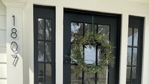A black front door with a wreath, a doormat with "you're here!" text, and a house number "1807".