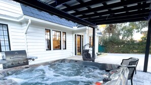 A hot tub in a covered outdoor area with a grill and chairs.