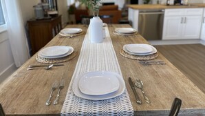 A dining table set with white plates, silverware, and a white vase with green plants.