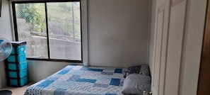 A bedroom with a bed, a window, a fan, and storage units. - Family Rest House (San Mateo)