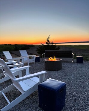 Terraza al aire libre con un pozo de fuego y altavoces, con el atardecer de fondo.