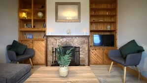 A living room with a fireplace, wooden shelves, a television, and two armchairs. - Cottage 427 - Clifden - sleeps 6 guests  in 3 bedrooms (Clifden)