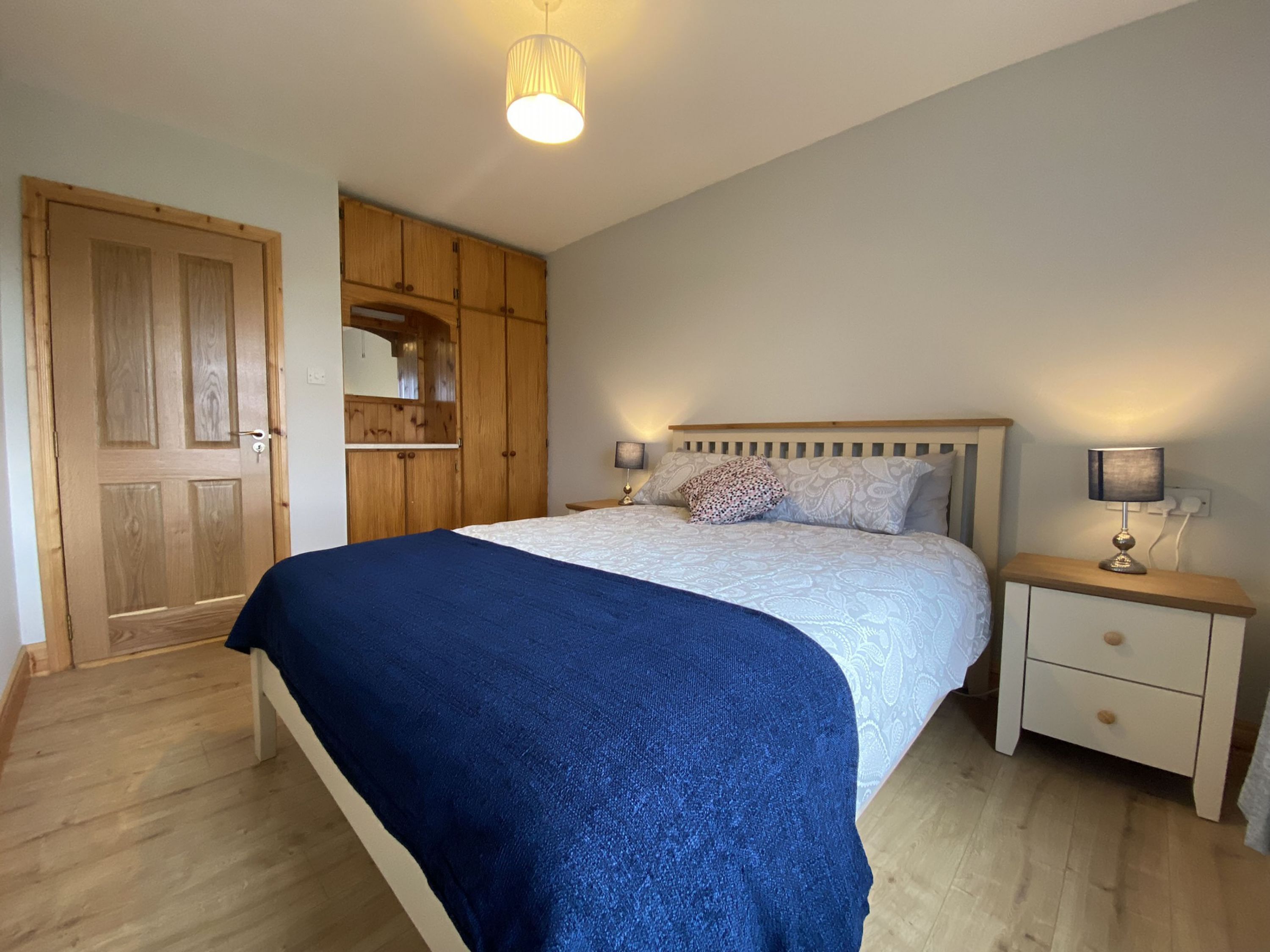 Une chambre à coucher comprenant un lit, des tables de chevet, une armoire et un luminaire suspendu.