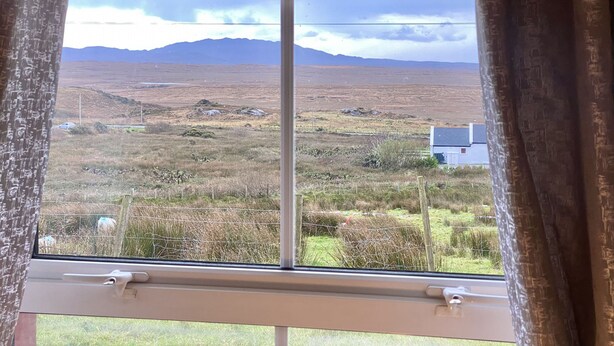 A window with a view of a rural landscape, including a house and distant mountains. - Cottage 427 - Clifden - sleeps 6 guests  in 3 bedrooms (Clifden)