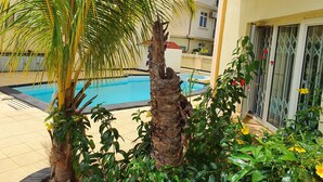 Ein Schwimmbecken, umgeben von tropischer Vegetation und einem Gebäude mit Balkon.