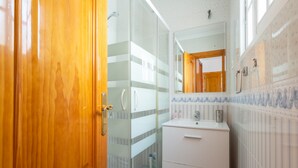 A bathroom with a wooden door, a glass shower enclosure, a white sink, and a mirror above it.