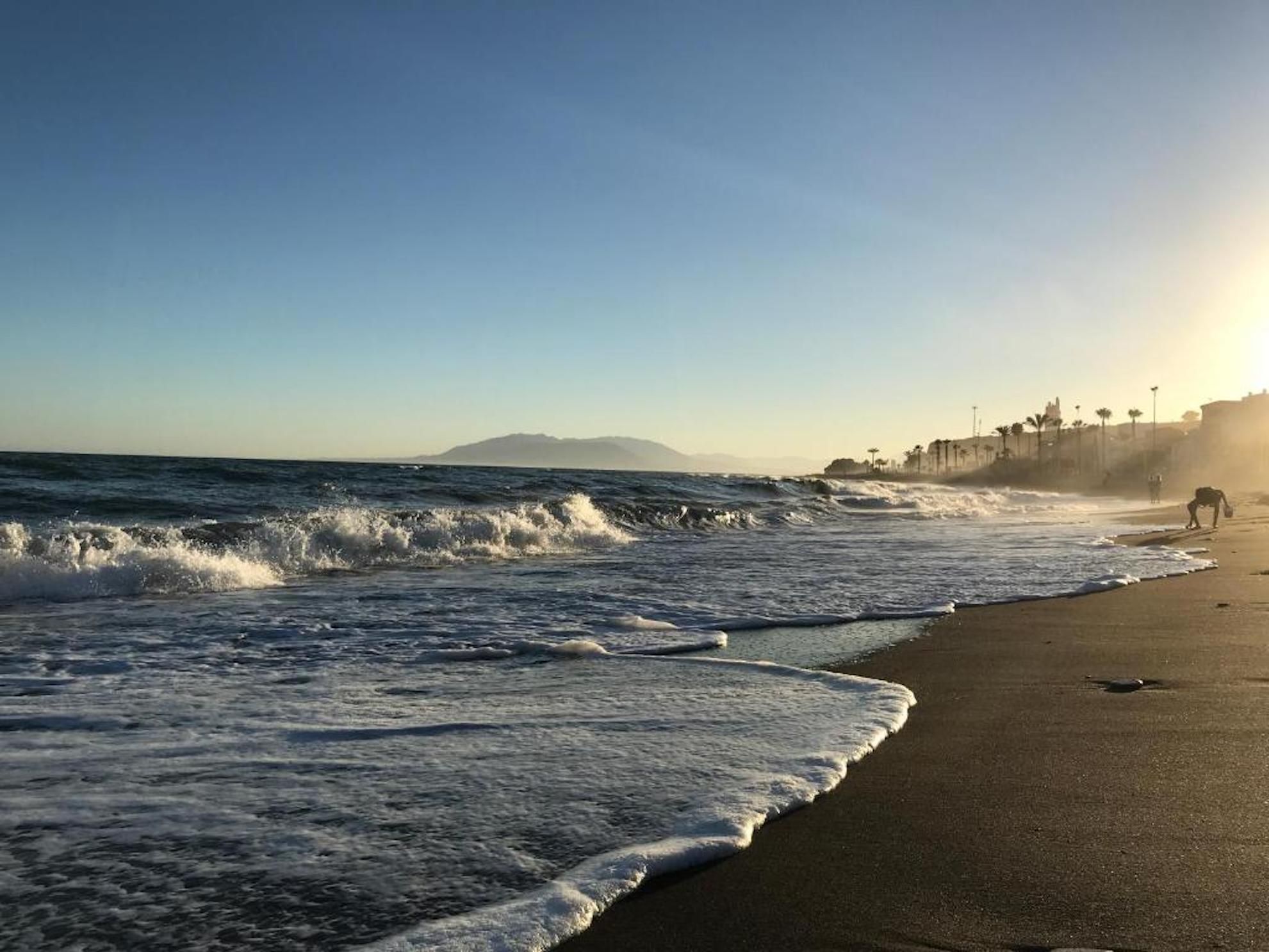 Ein Strand mit Wellen, einem klaren Himmel und einem entfernten Berg.