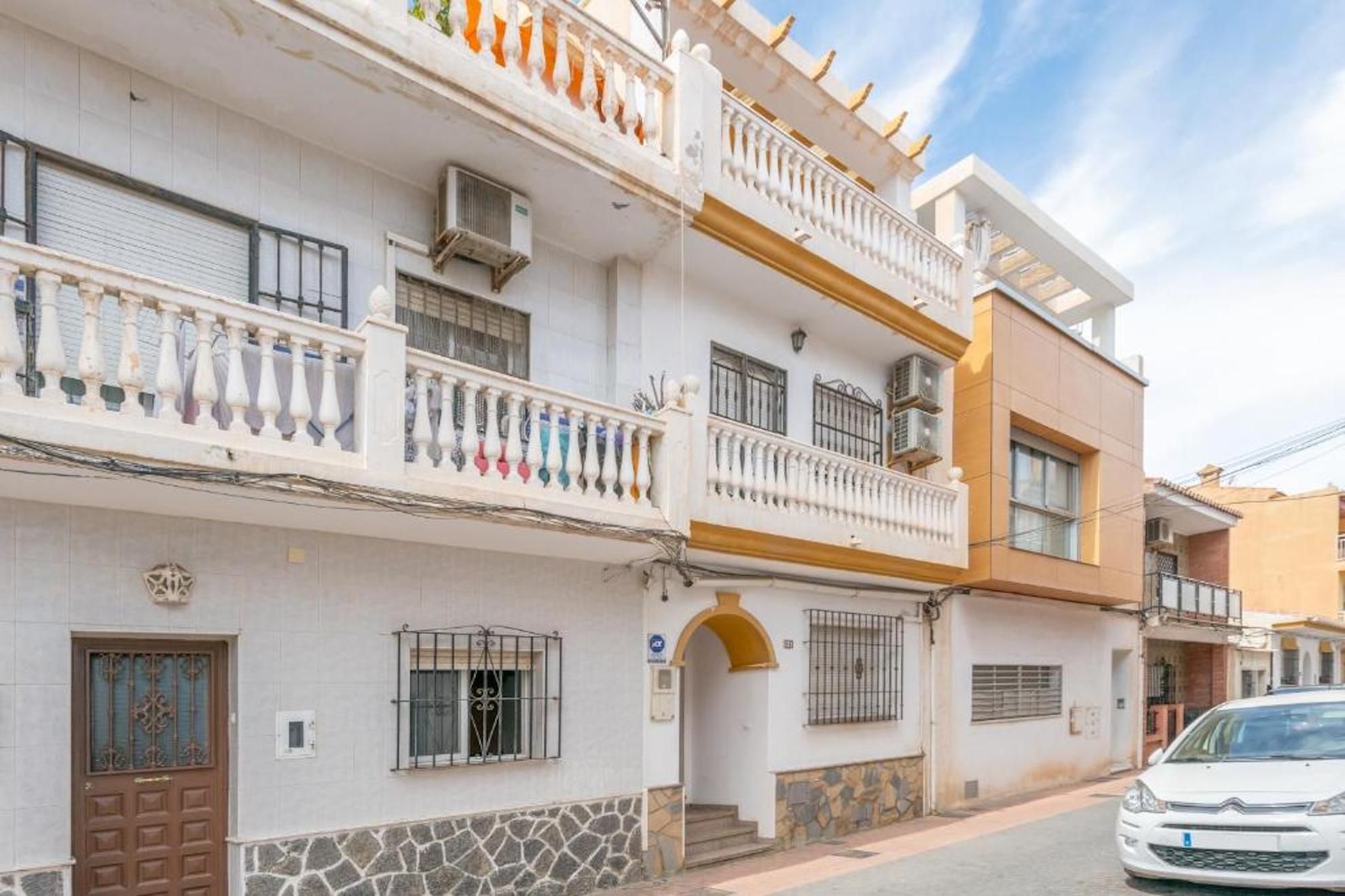 Un edificio residencial de varios pisos con balcones, unidades de aire acondicionado y un coche estacionado adelante.