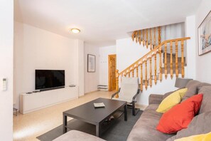 A living room with a sofa, a coffee table, a TV, and a staircase. - RENTS Victoria Beach (La Cala Del Moral Rincon de la Victoria)