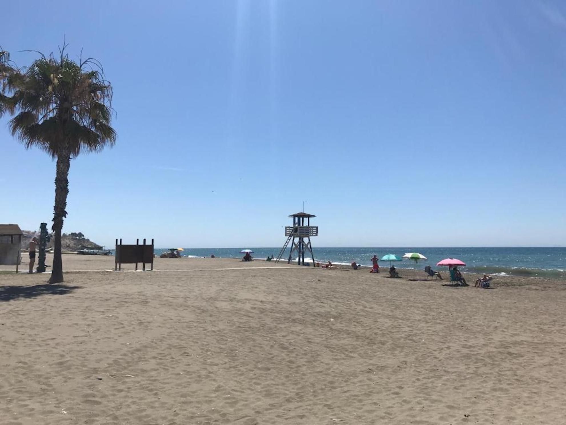 A beach with a lifeguard tower, palm trees, and umbrellas.