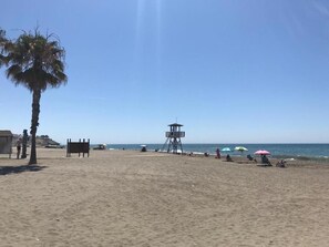 A beach with a lifeguard tower, palm trees, and umbrellas. - RENTALS Victoria Beach (La Cala Del Moral Rincon de la Victoria)