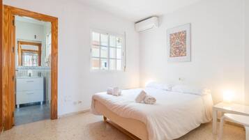 Een slaapkamer met een bed, een raam, een airconditioning en een klein tafeltje.