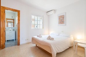 A bedroom with a bed, a window, an air conditioning unit, and a small table.