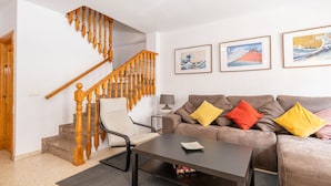 A living room with a wooden staircase, a sofa with colorful cushions, and framed artwork on the wall.