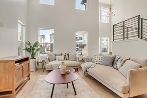 Un salon spacieux avec un grand canapé, une table basse en bois et une vue sur la ville grâce à de grandes fenêtres.