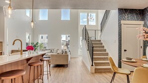Un grand espace de vie comprenant une cuisine, des tabourets de bar, un escalier et une table à manger avec des chaises.