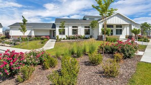 Une maison moderne à deux étages, dotée d’un jardin bien entretenu, comprenant des plantes à fleurs et des arbustes.
