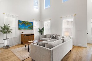 Un salon spacieux avec un grand canapé, un meuble en bois et un tableau représentant une plage tropicale.