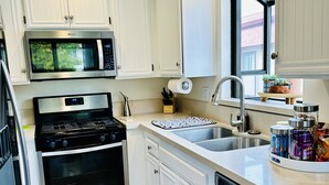 Una cocina moderna con armarios blancos, electrodomésticos de acero inoxidable, piso de madera y ventana con vistas.