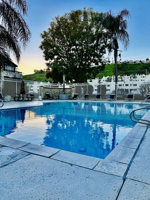 A swimming pool with lounge chairs and umbrellas, surrounded by a white fence and trees.