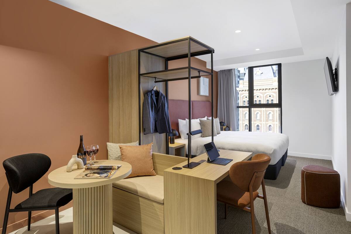 A modern hotel room with a bed, a desk, a chair, a round table, and a small ottoman.