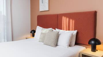 A neatly made bed with white linens and a textured pillow, a bedside lamp, and a framed abstract artwork on the wall.
