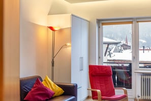 Una habitación moderna con sofá, una silla roja, una lámpara de pie, una ventana con vistas a un paisaje nevado y un radiador.