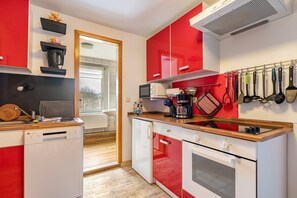 Uma cozinha compacta com armários vermelhos e brancos, uma lava-louças, um micro-ondas e uma cafeteira.