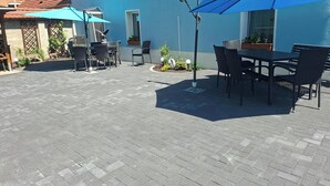 Un patio al aire libre con mesas y sillas, un paraguas azul y plantas en macetas.